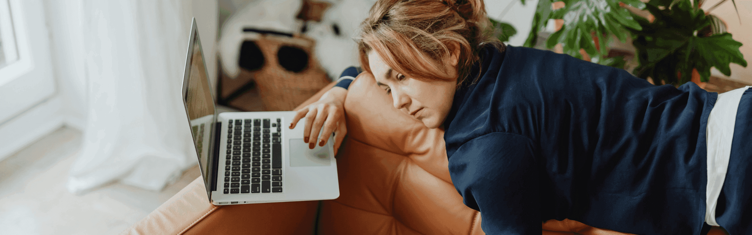 Junge Frau liegt auf dem Sofa und blickt frustriert auf einen Laptop