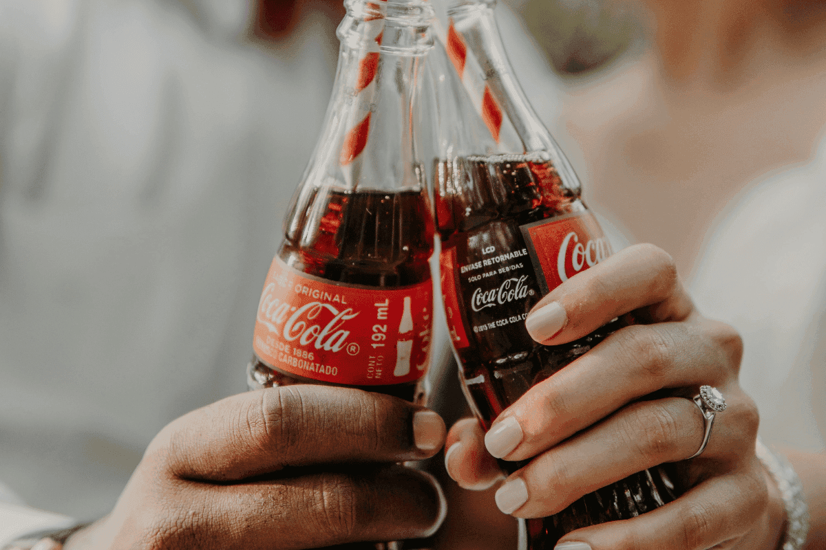 Zwei Personen stoßen mit klassischen Coca-Cola-Flaschen an, Nahaufnahme der Hände