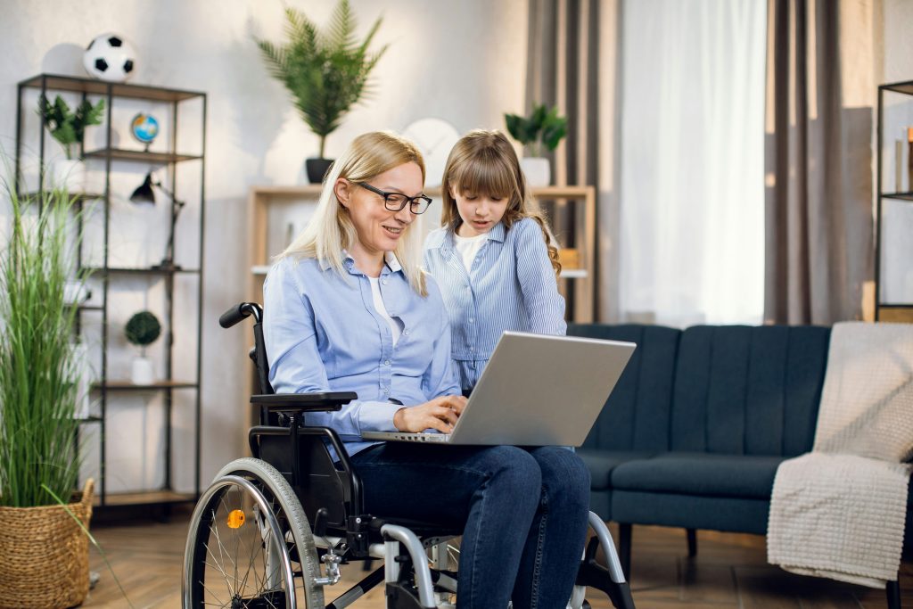 Frau im Rollstuhl sitzt mit einem Kind vor einem Laptop.